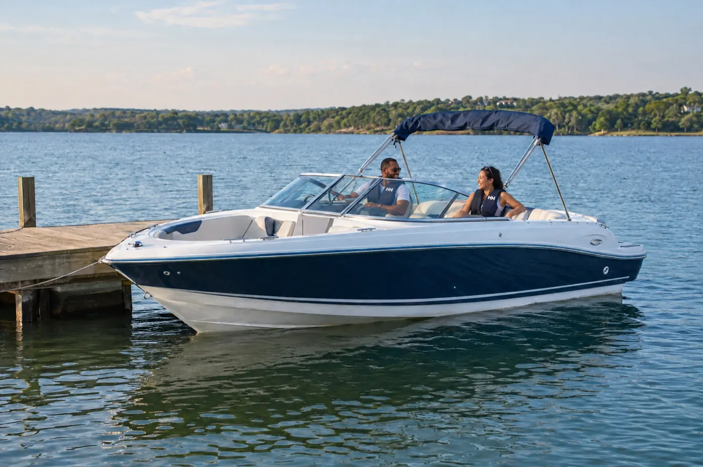 A couple wearing life jackets aboard a blue and white bowrider on a calm lake