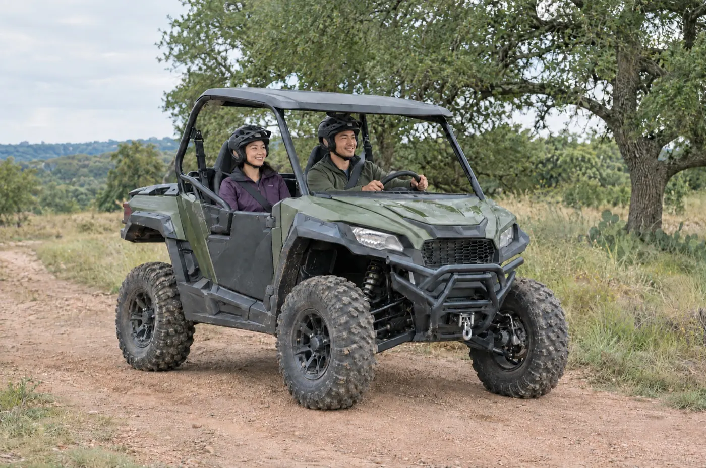 A couple wearing helmets driving an olive green side-by-side on a Texas trail
